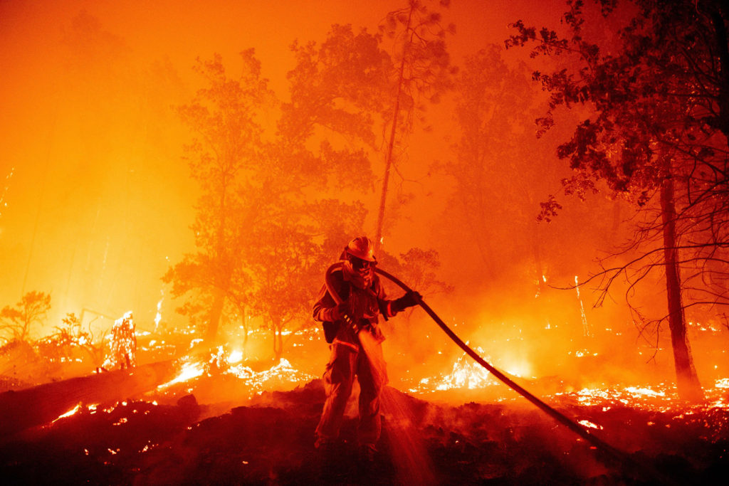 Image of firefighter surrounded by smoke and flames putting out forest fire.