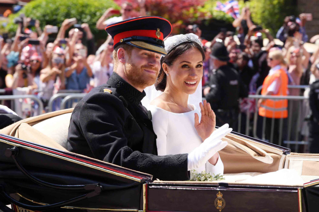 Prince Harry and Meghan Markle waving to fans, leaving their wedding in a carriage
